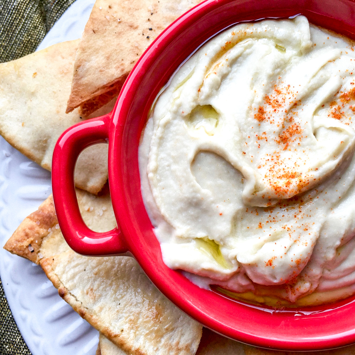 white bean dip in red serving dish surrounded by seasoned pita chips