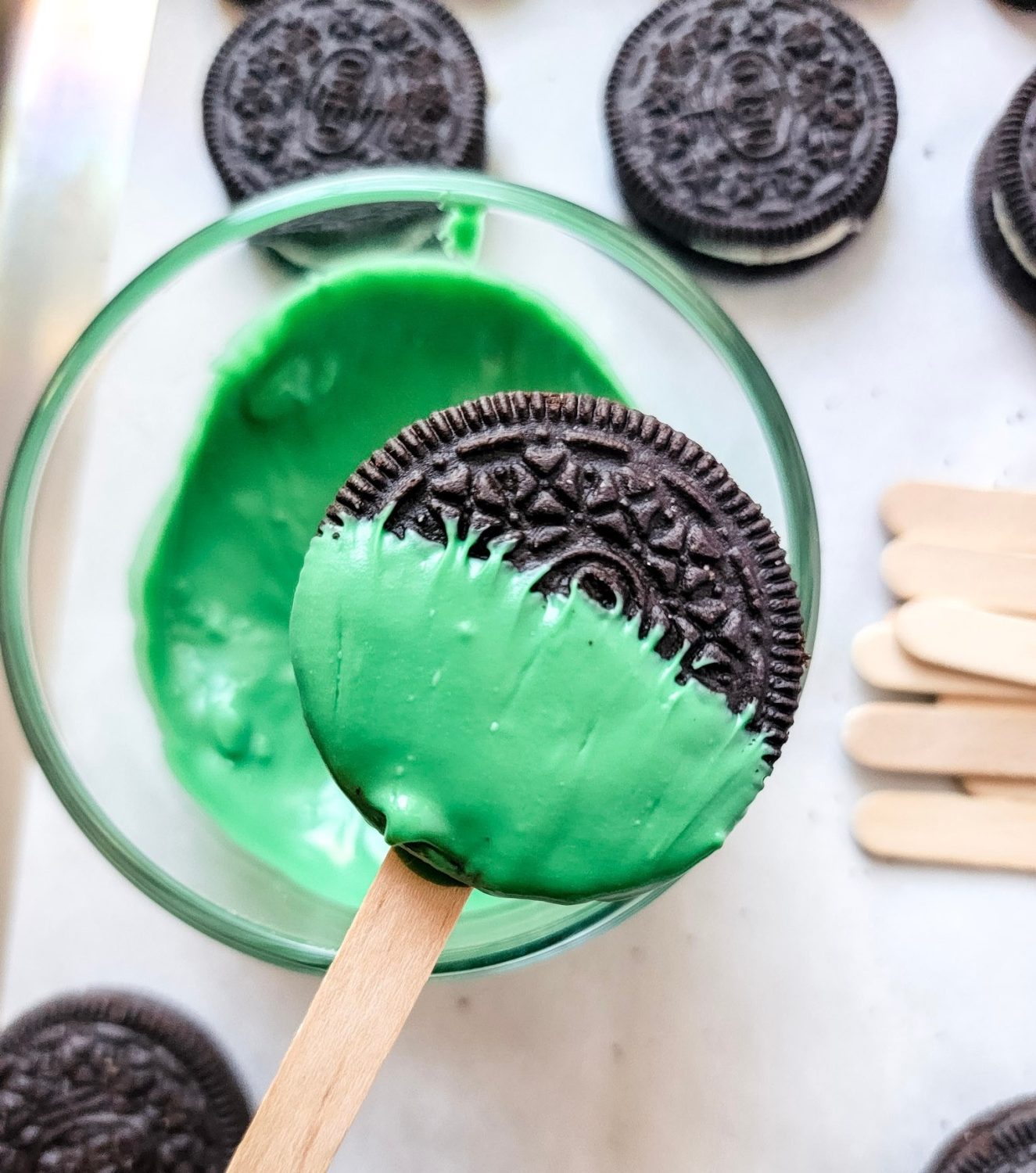 oreo dipped in green chocolate to make holiday mickey mouse oreo pops