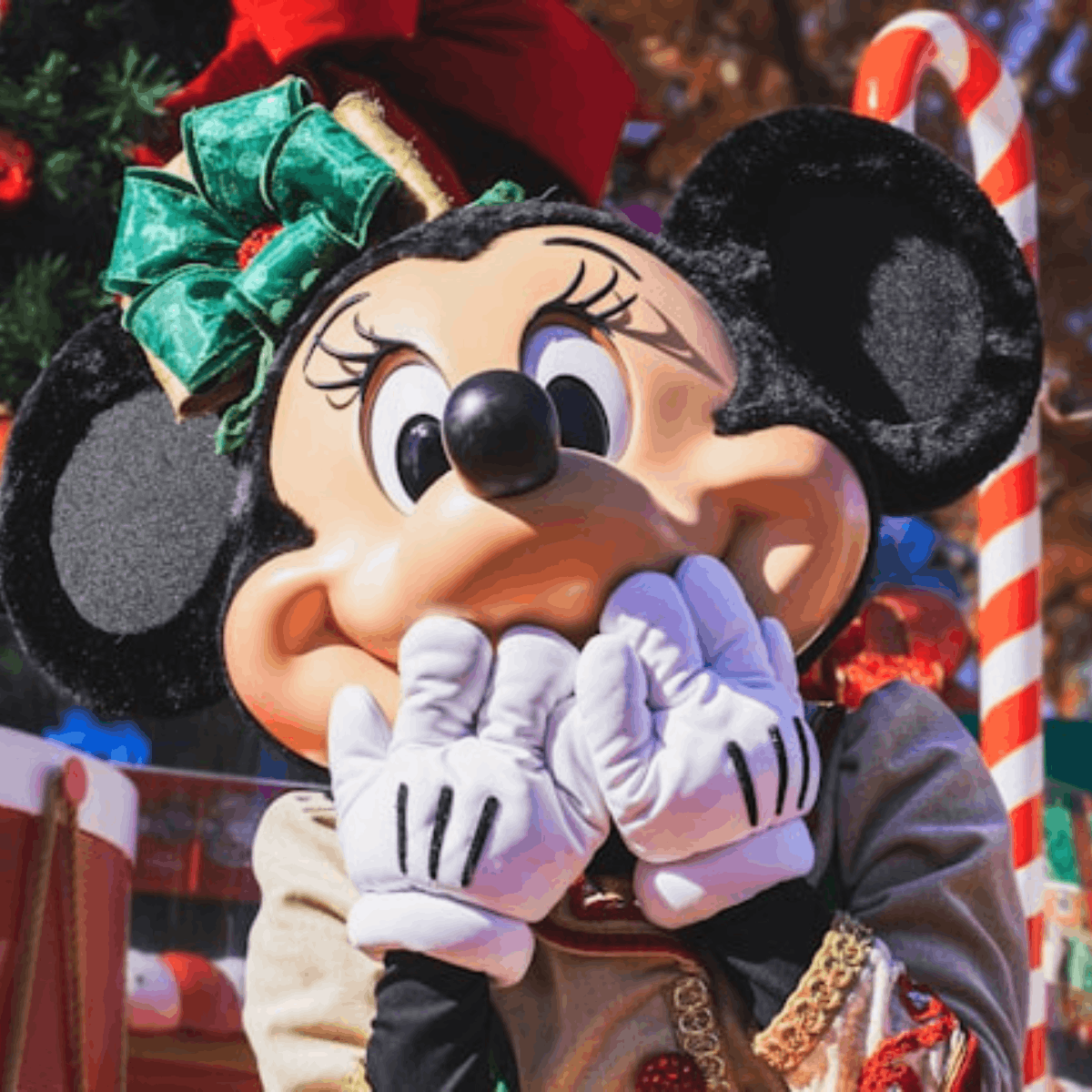 Close-up of Minnie Mouse wearing a green bow, covering her mouth with white gloves during a holiday parade scene.