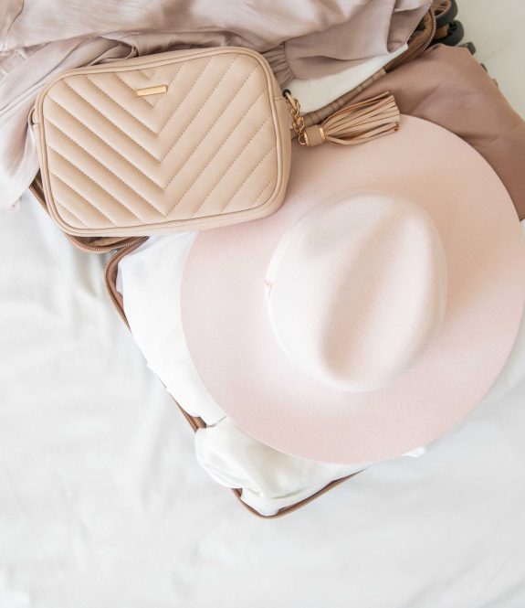 packing suitcase with pink hat and tan crossbody bag
